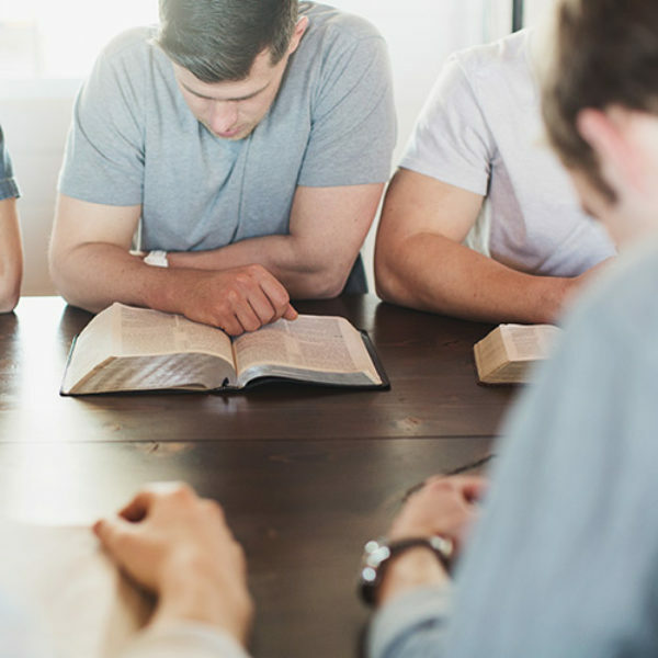 group of men sitting at a table, reading Bibles